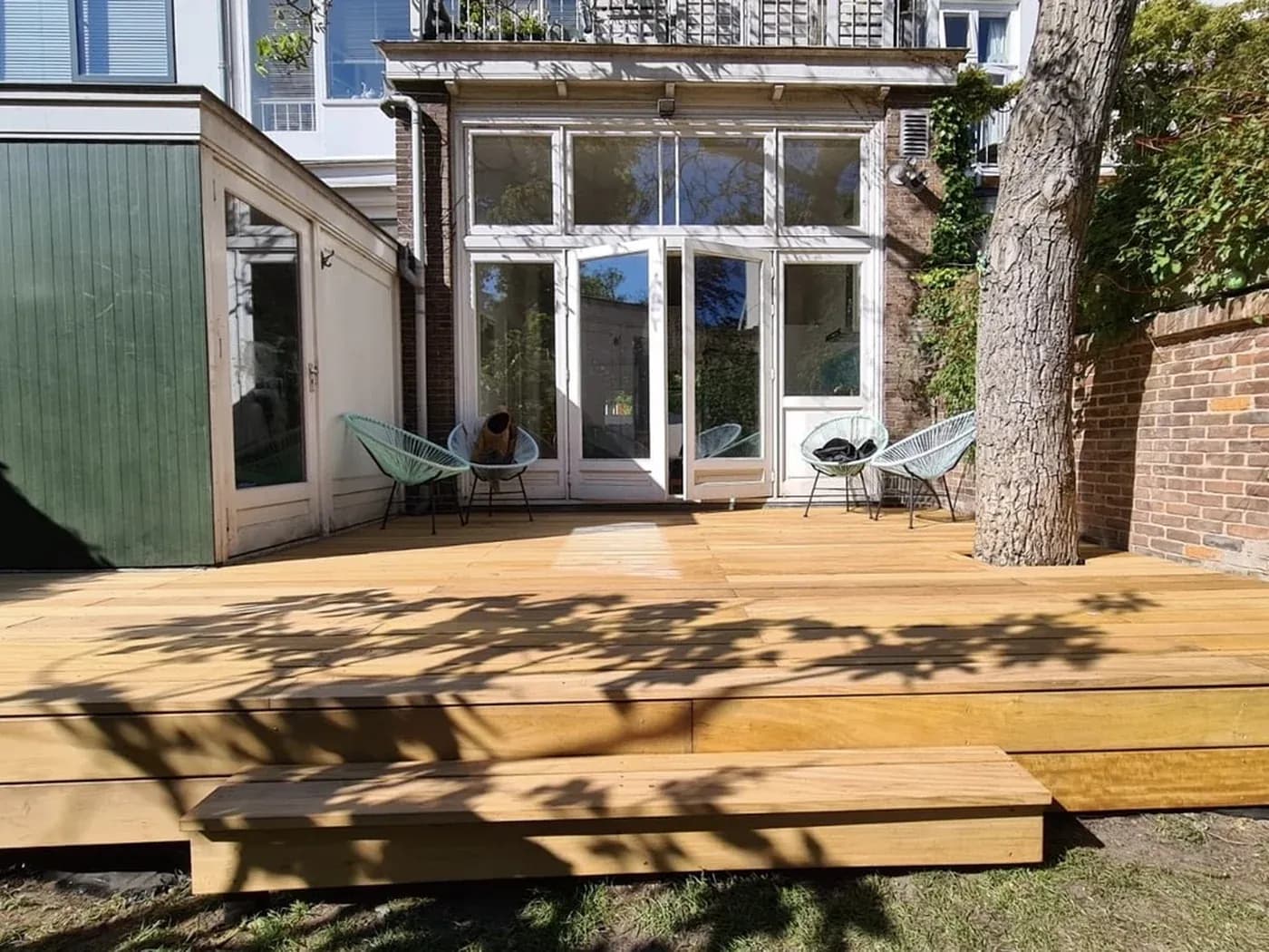 Nieuw hardhouten vlonderterras met brede traptreden rond de bestaande boom in de Huijgensstraat, Den Haag